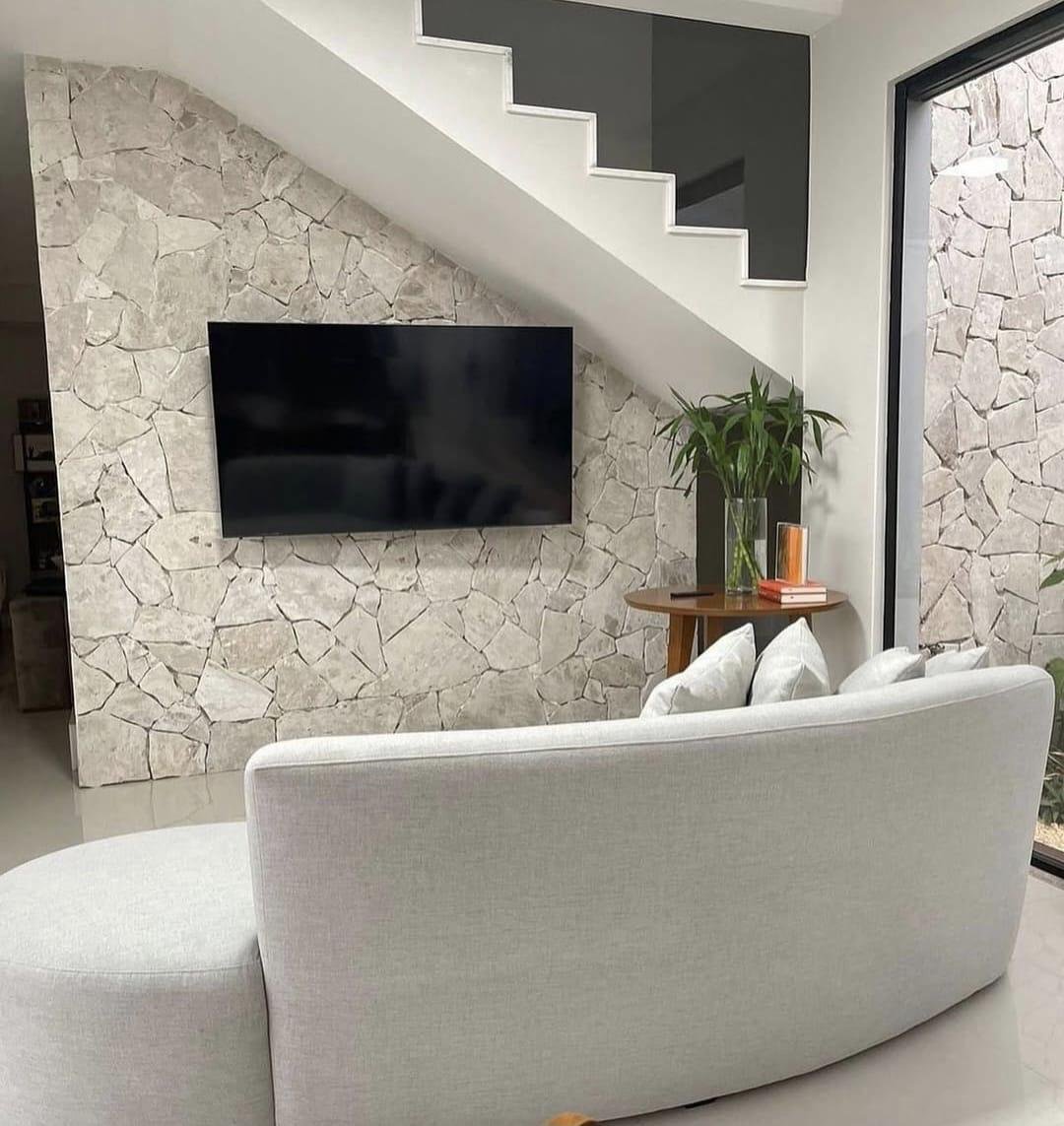 Sala com poltronas verdes e parede de pedra irregular
